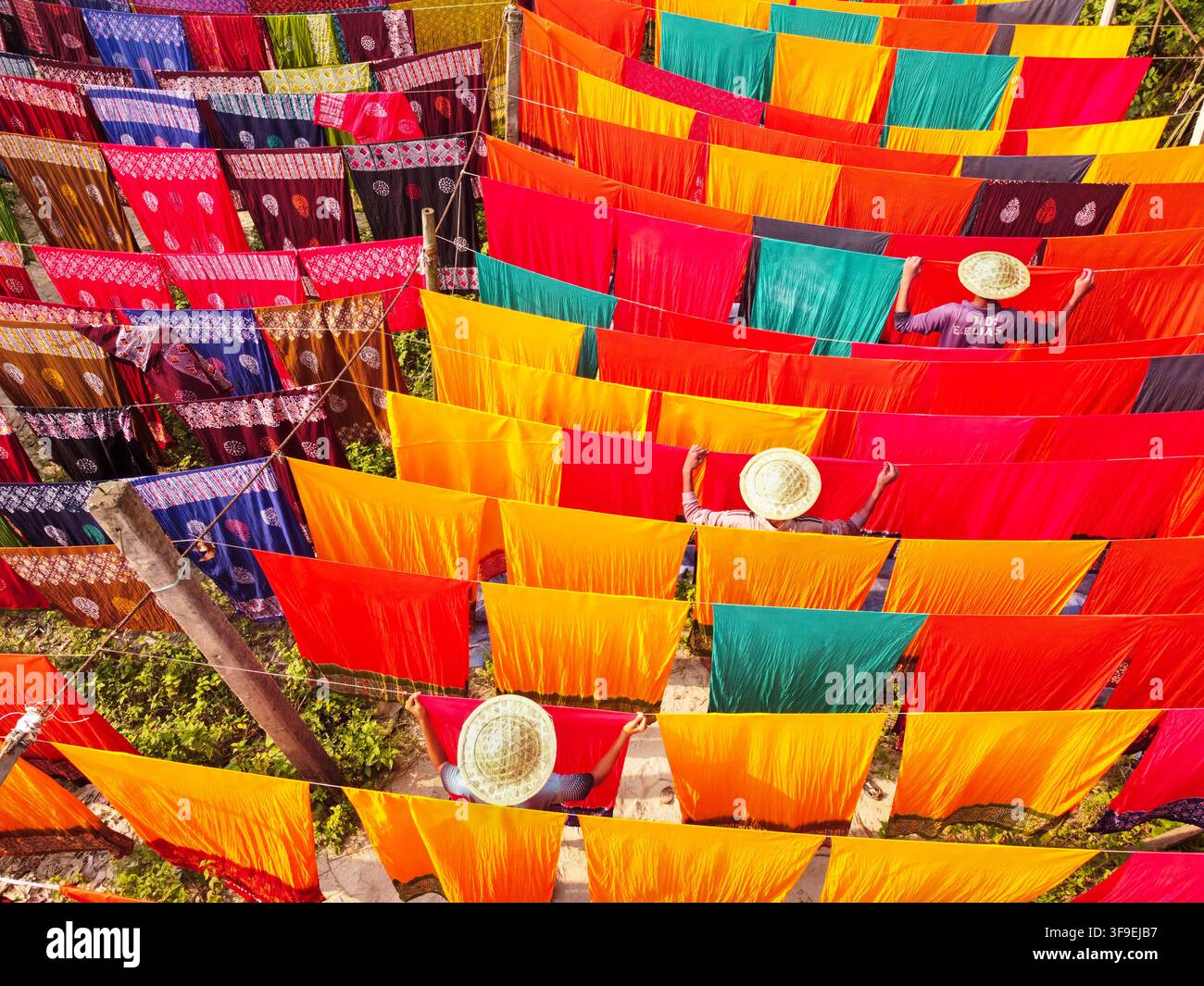 Vista aerea di tessuti colorati in asciugatura con lavoratori che indossano cappelli a cono e appendono tessuti vivaci ad asciugare al sole a Narayanganj, Divisione di Dacca, Ba Foto Stock
