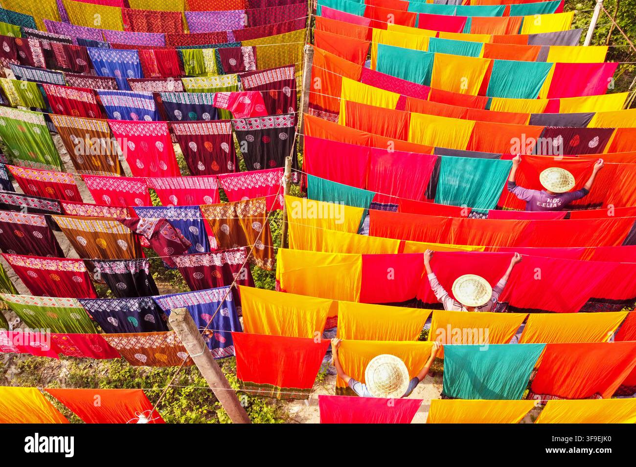 Veduta aerea di tessuti colorati che asciugano al sole con lavoratori che indossano cappelli di paglia e appendono tessuti a Narayanganj, Divisione di Dhaka, Bangladesh. Foto Stock