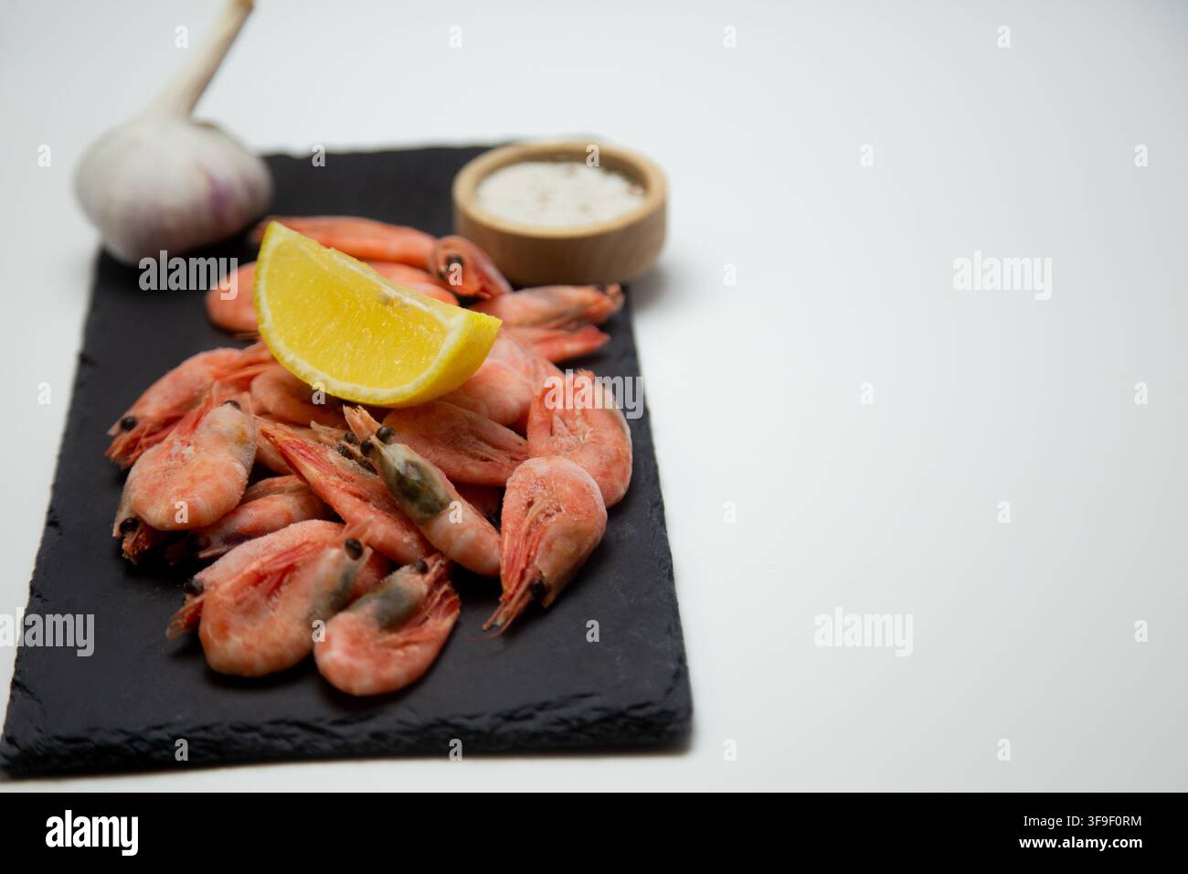 Su un ardesia nera con gamberetti congelati, sopra i quali si trova mezza limone, aglio e una saliera Foto Stock