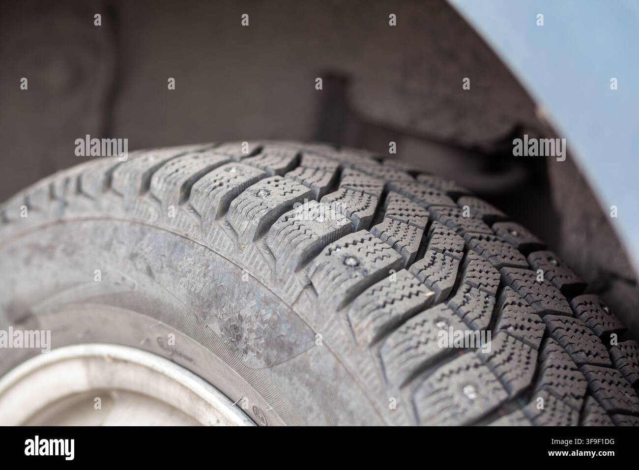 Vista ravvicinata di uno pneumatico invernale consumato che mostra i motivi del battistrada e i dettagli della parete laterale, montato su un veicolo in un ambiente di garage Foto Stock