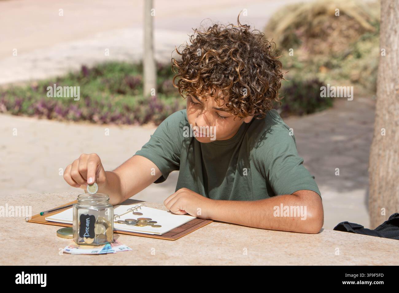 Ragazzo che risparmia monete in un barattolo per un sogno. L'immagine rappresenta la alfabetizzazione finanziaria, le abitudini di risparmio e la fissazione di obiettivi tra i giovani. Foto Stock