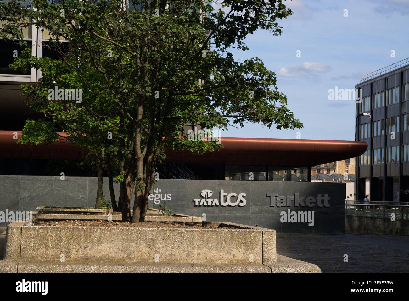Insegne aziendali tra cui Tata Consultancy Services, Regus e Tarkett su sfondo di edifici moderni della città e verde urbano. Foto Stock