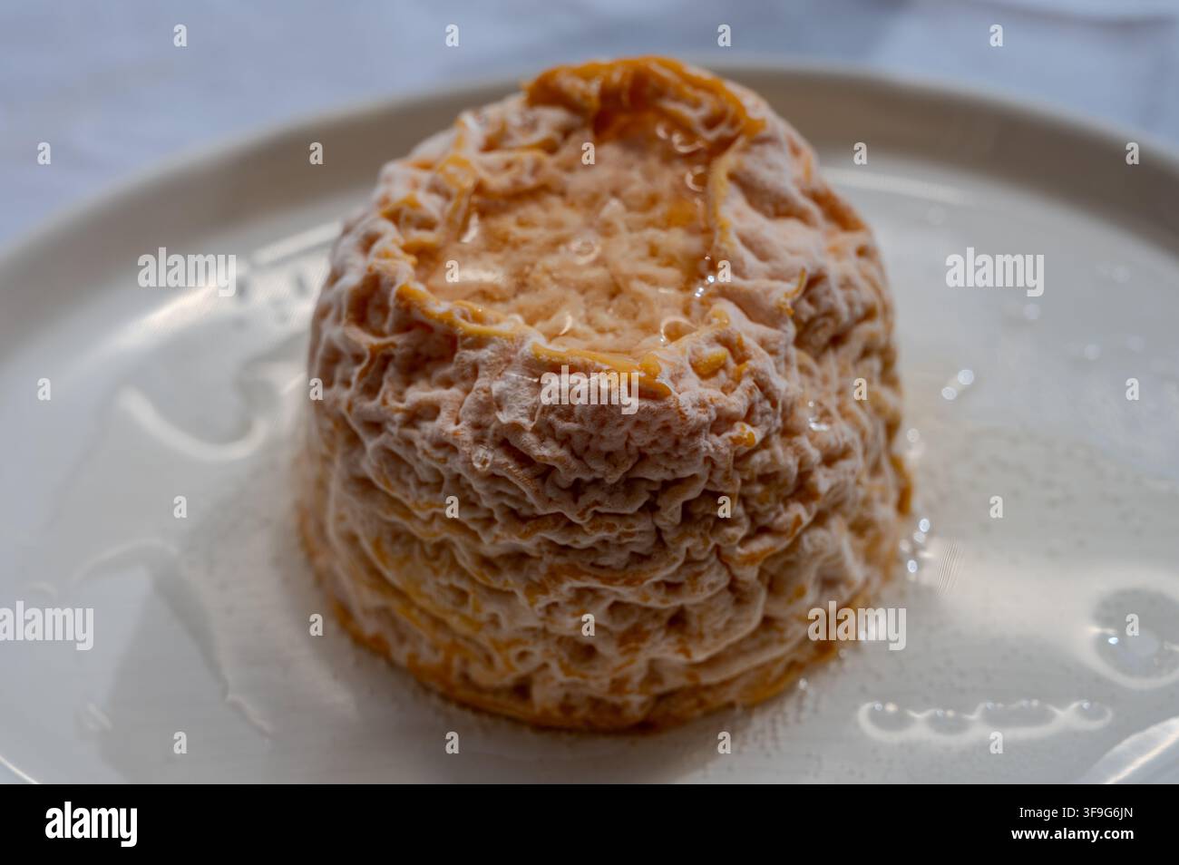 Piccolo formaggio Lsoft francese Langres rotondo con crosta lavata all'arancia e centro cremoso su un tavolo, cucchiaio e abbinato a champagne Foto Stock