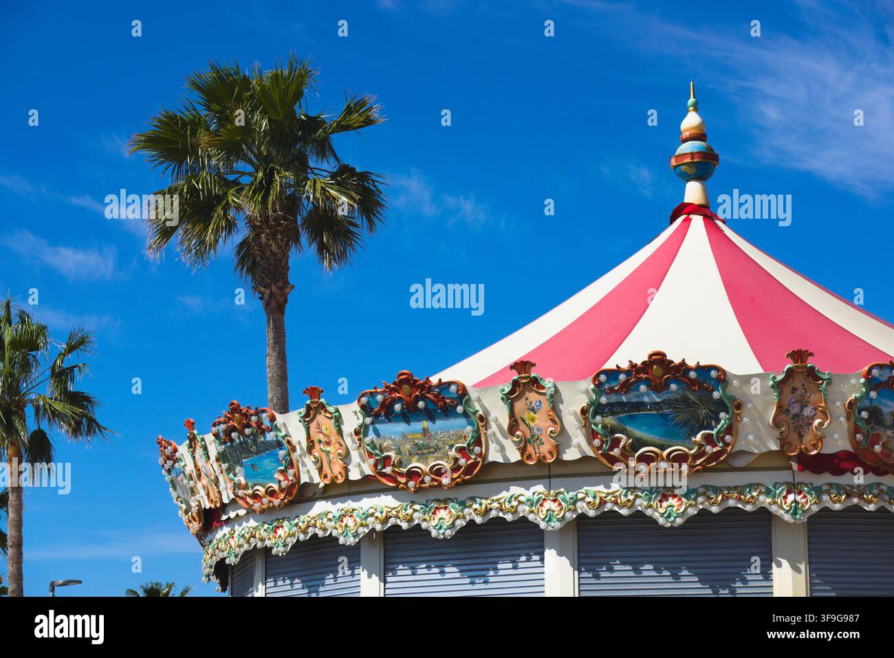 Un tetto di giostra vintage sormontato da un pinnacolo accanto a una palma contro un cielo blu a La Ciotat, Costa Azzurra, Francia. Foto Stock