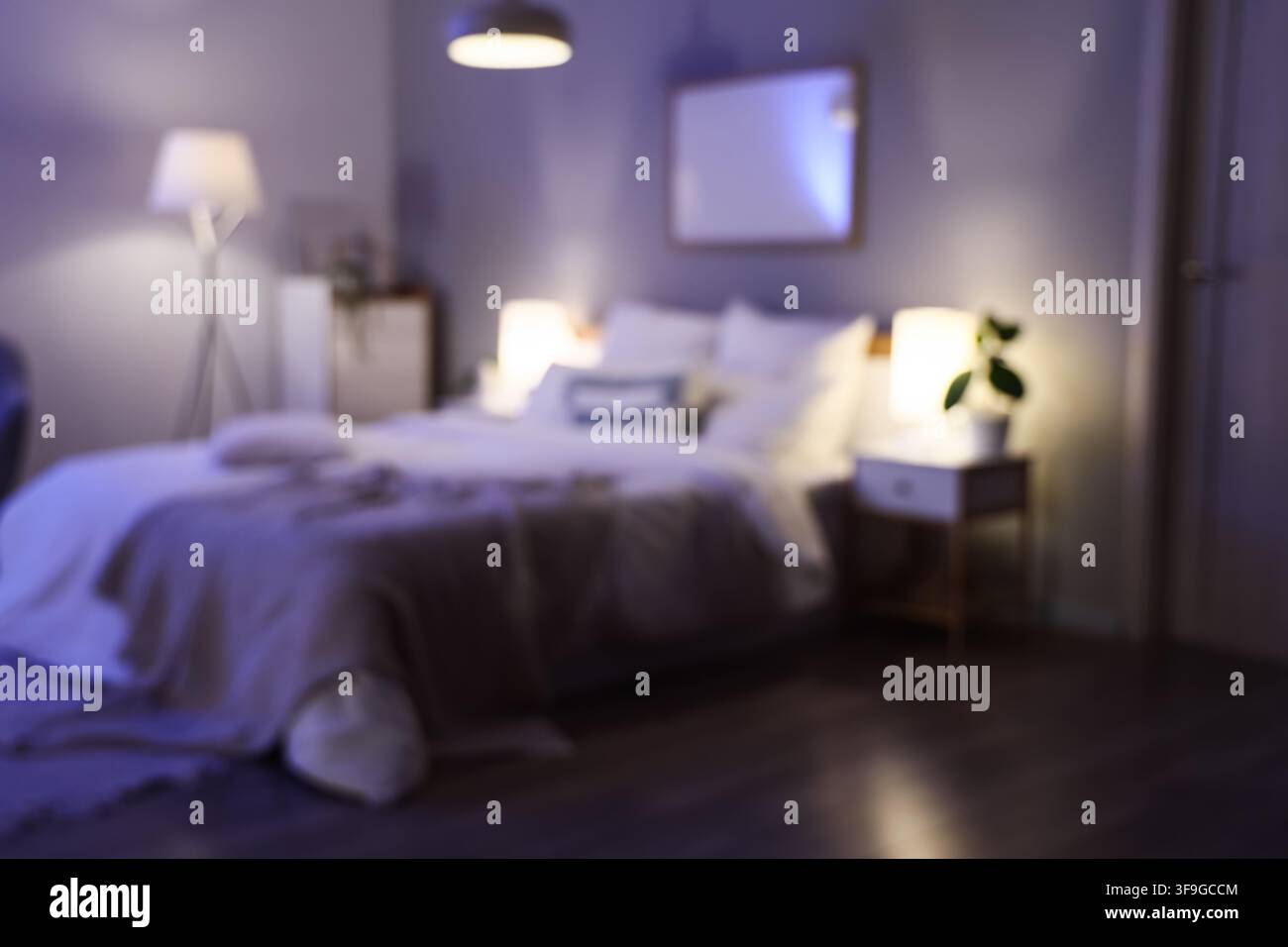 Interno di camera da letto sfocato con illuminazione soffusa, atmosfera accogliente e letto comodo per il relax e il sonno Foto Stock