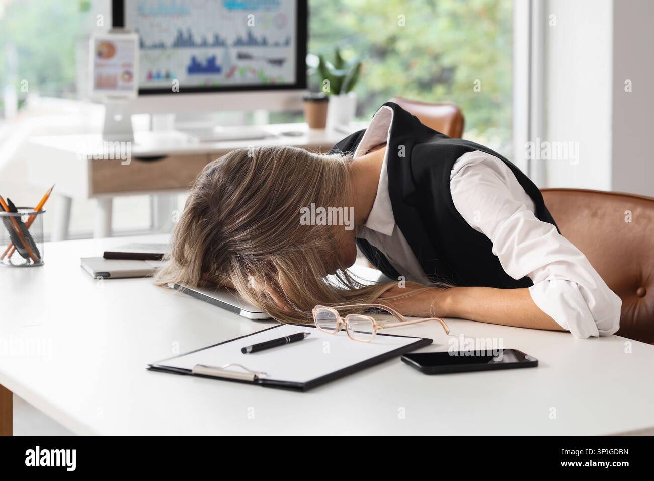 Donna d'affari esausta che dorme sul laptop alla scrivania dell'ufficio, concetto di burnout e sovraccarico, stress e stanchezza nell'ambiente aziendale Foto Stock
