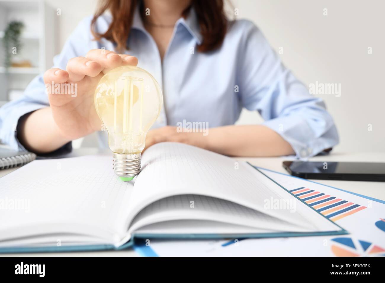Donna d'affari che tiene una lampadina sopra un quaderno aperto nuove idee innovazione e risoluzione creativa dei problemi nella donna d'affari Foto Stock