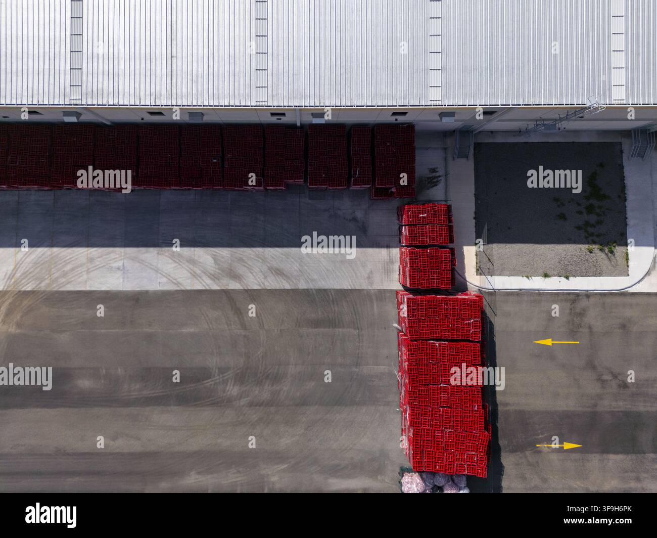 Vista aerea di un centro logistico con pile di casse rosse sull'asfalto, frecce direzionali gialle e un grande tetto industriale a Santiago de Foto Stock