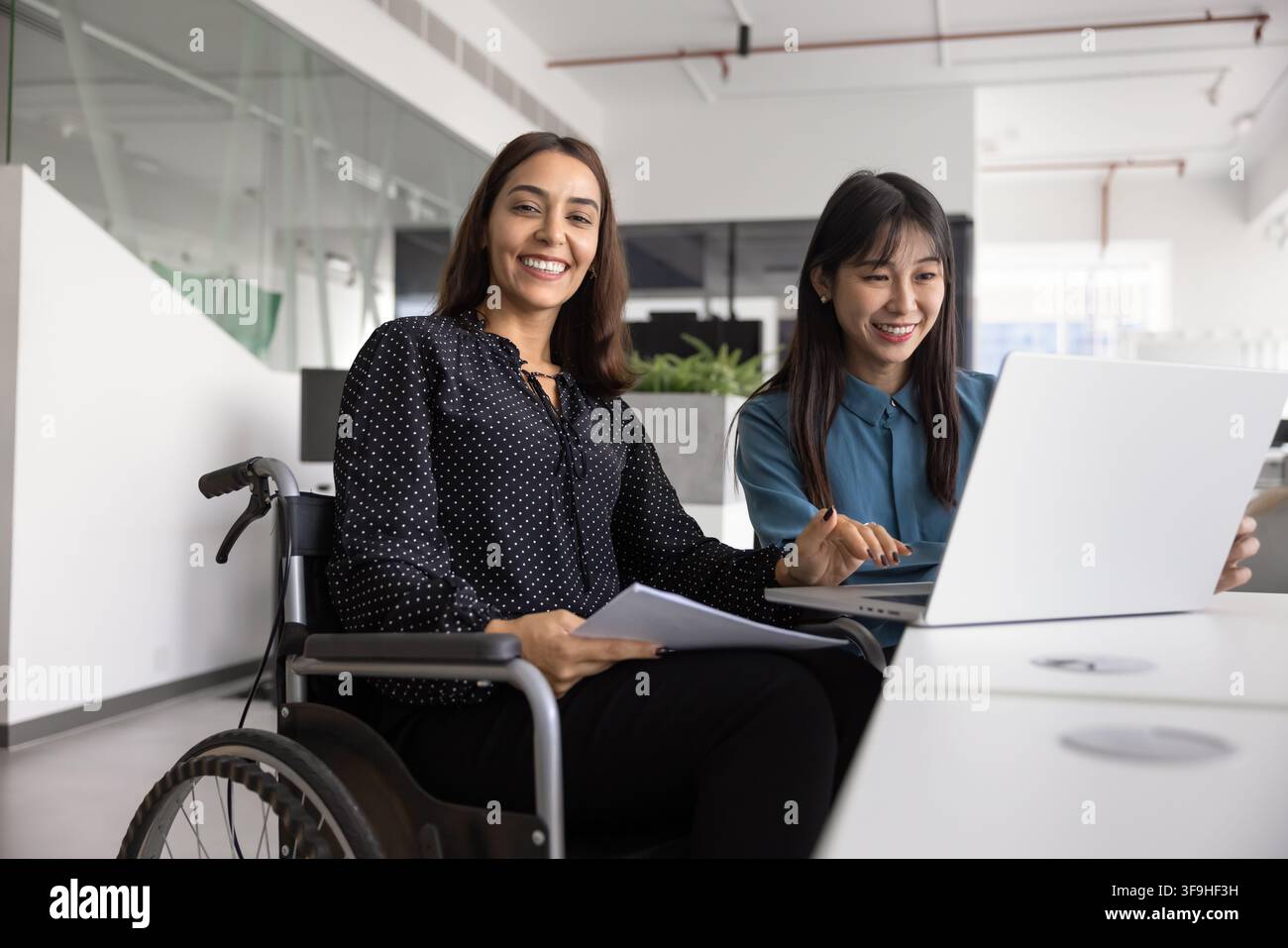 Donna in sedia a rotelle che lavora con una collega donna in ufficio Foto Stock