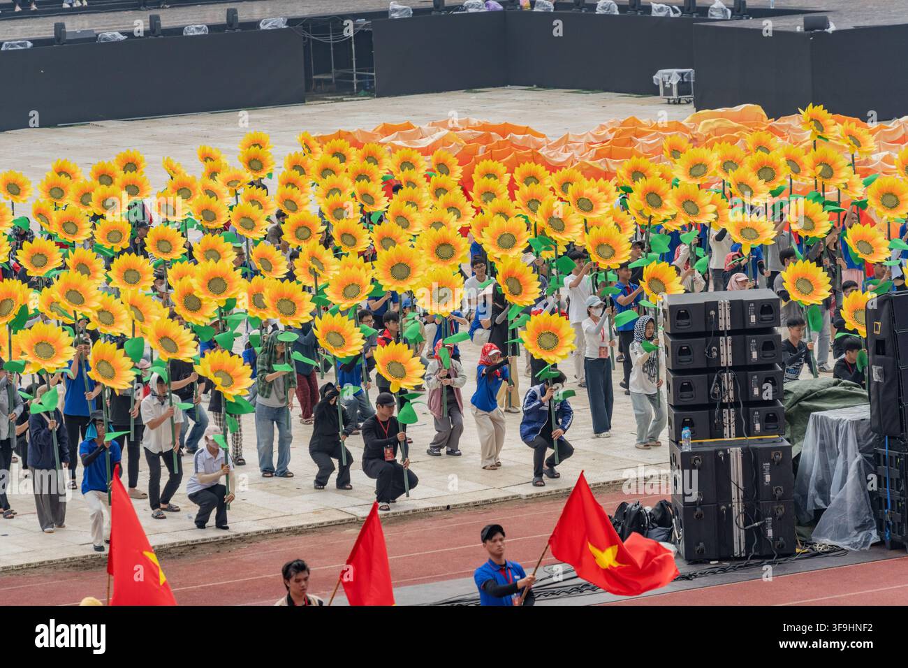 Vista aerea di interpreti che tengono giganteschi oggetti di scena a forma di girasole in formazione ondulata, Stadio My Dinh, Hanoi Foto Stock