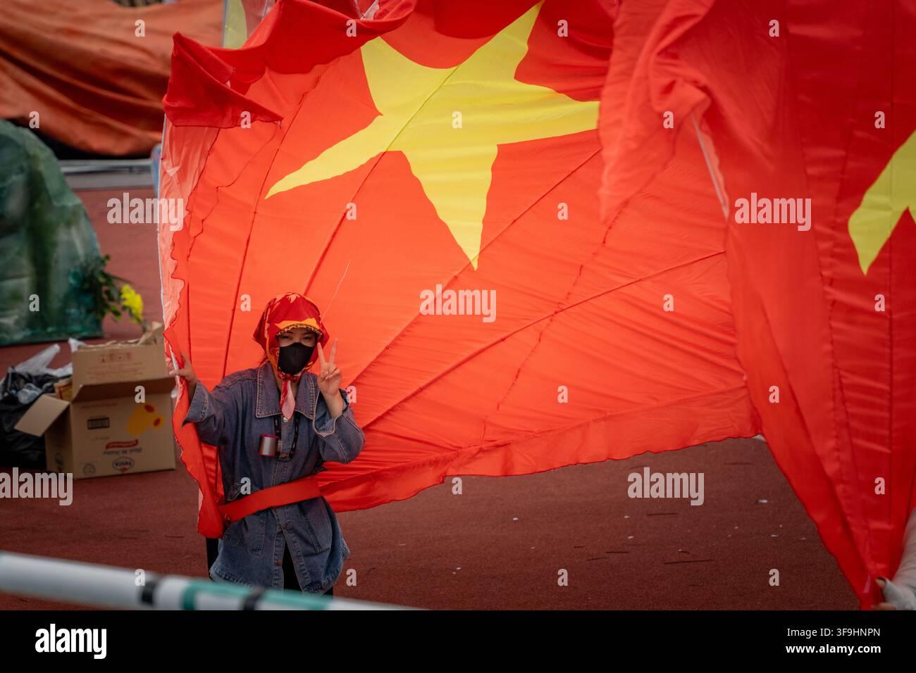 Giovane artista che fa il segno della pace mentre è avvolto in un enorme accessorio a forma di bandiera vietnamita, Stadio My Dinh, Hanoi Foto Stock
