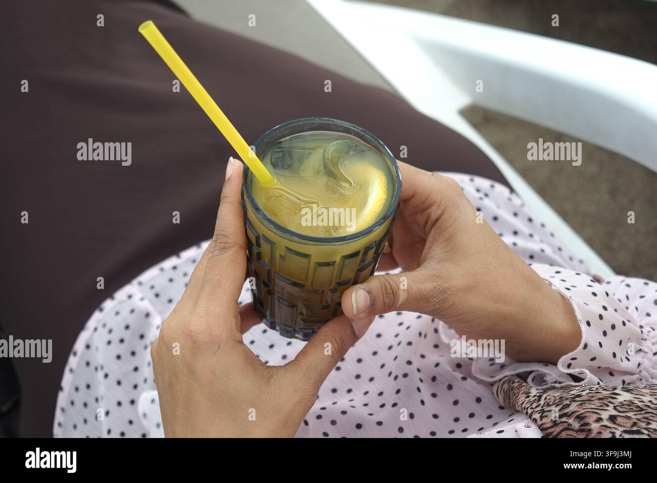 una persona che tiene un bicchiere pieno di una bevanda fredda miscelata giallo-verde e una cannuccia gialla Foto Stock