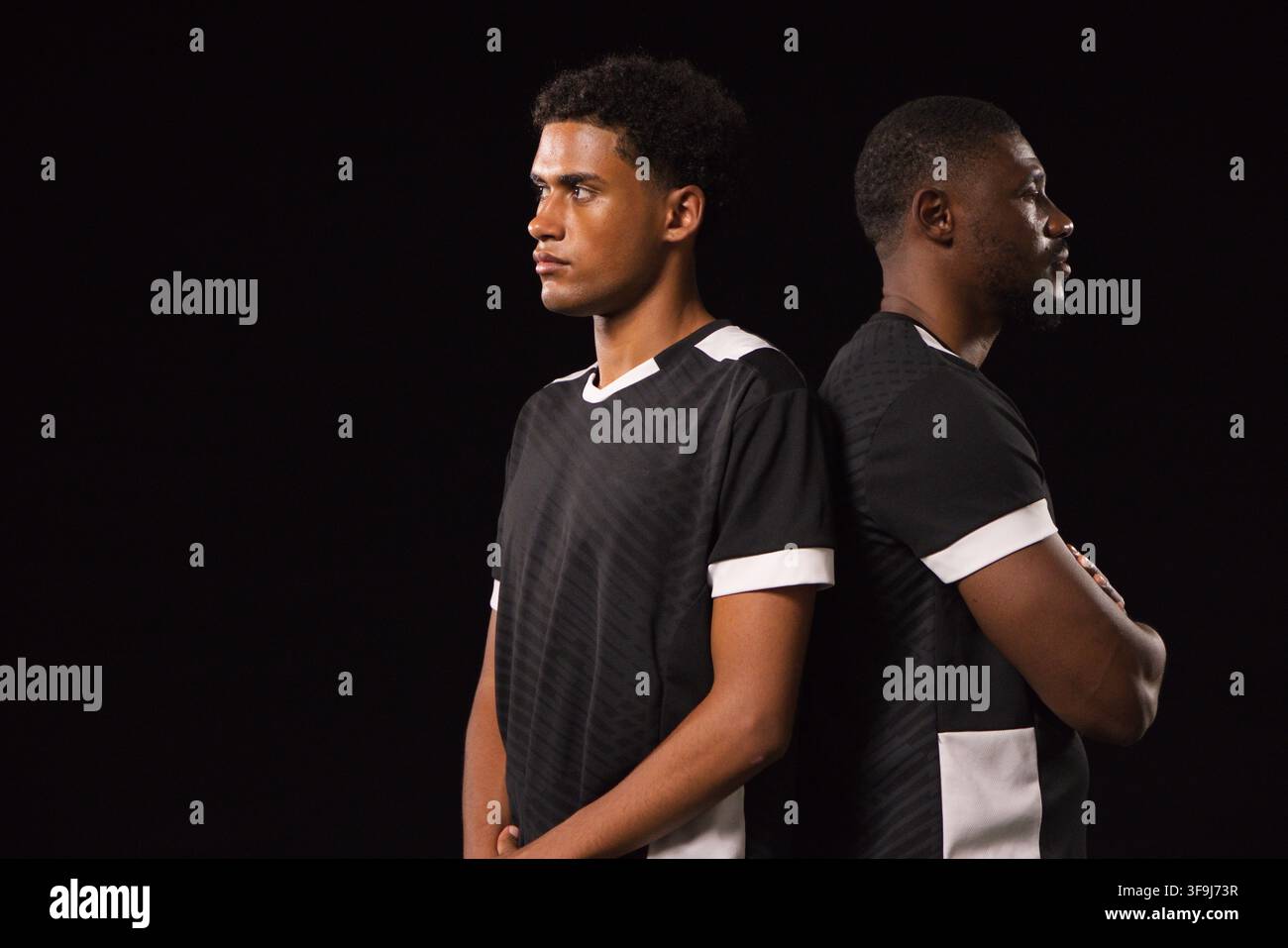 Uomini afroamericani in piedi schiena contro schiena in studio che indossano maglie nere coordinate con rifiniture bianche Foto Stock