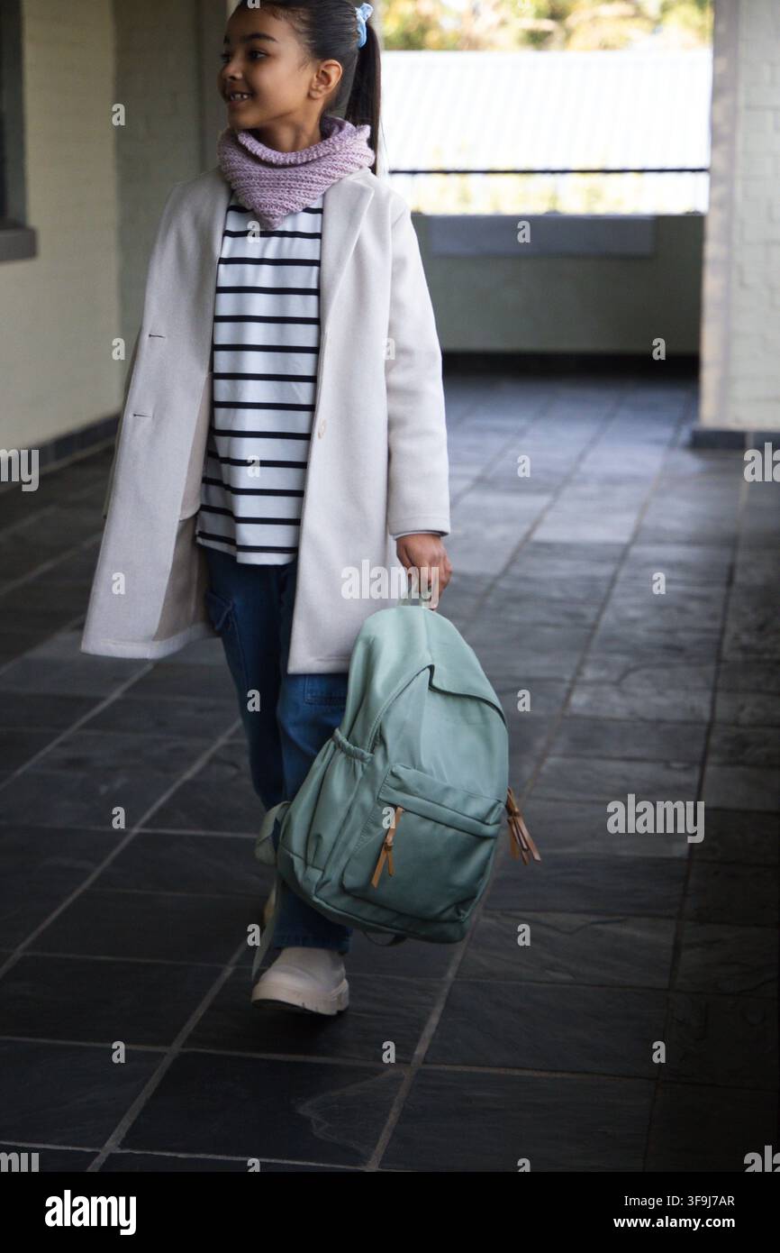 Adolescente afroamericano con giacca chiara che cammina attraverso una passerella coperta portando uno zaino verde menta Foto Stock