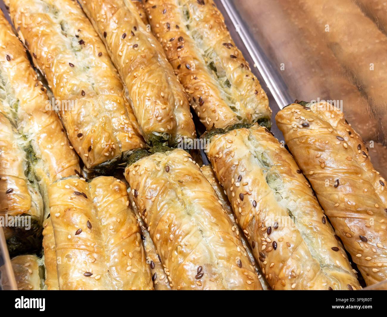 Rotoli di spinaci dorati e croccanti disposti in un contenitore metallico da esposizione, offrendo una deliziosa scelta di pasticcini salati per pasti mattutini gourmet, snack o Foto Stock