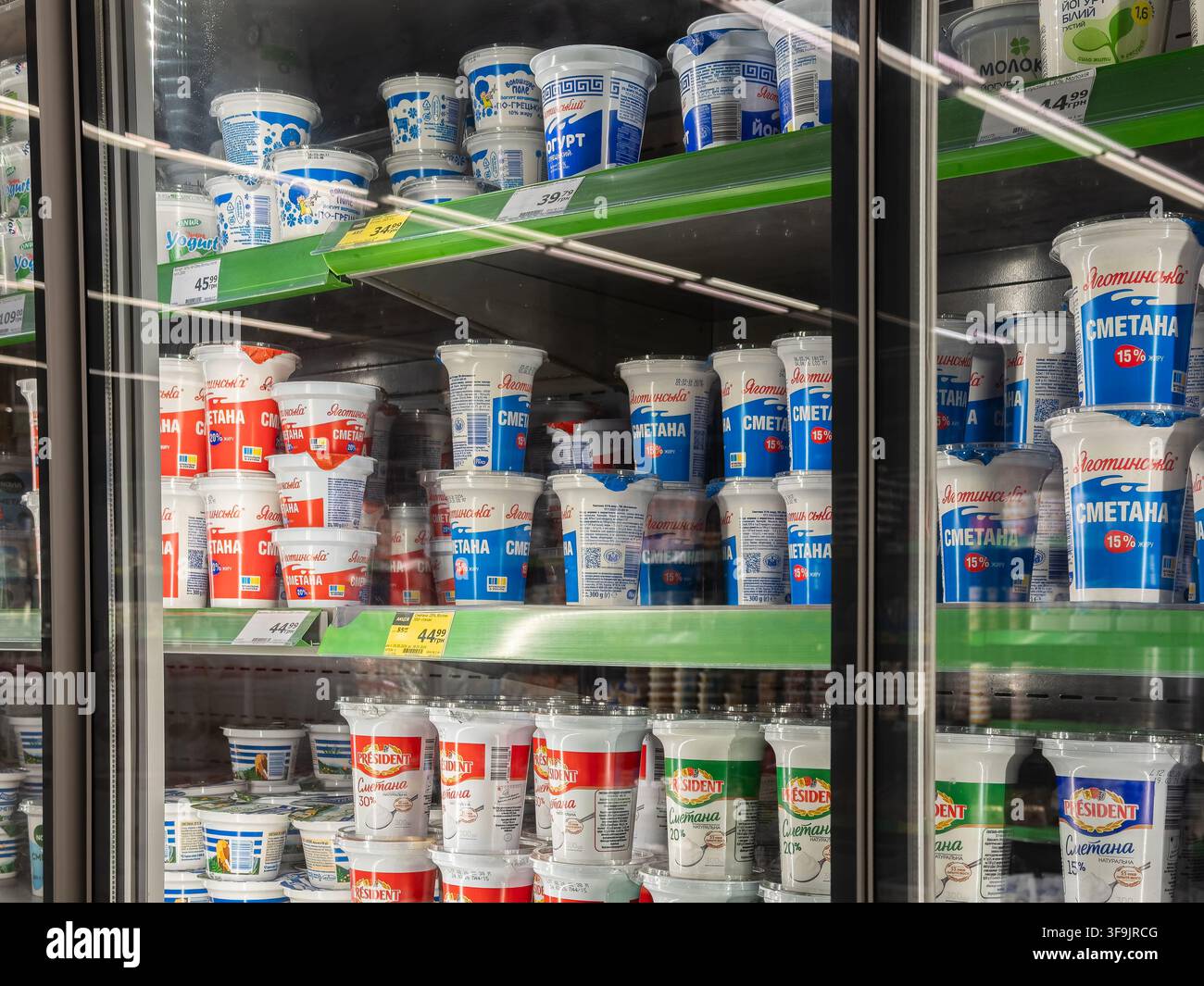 Kyiv, Ucraina - 14 marzo 2026: vasetti di panna acida Yagotynske e yogurt President impilati all'interno di un'espositore refrigerata di un supermercato, rappresentanti dei dai sani Foto Stock
