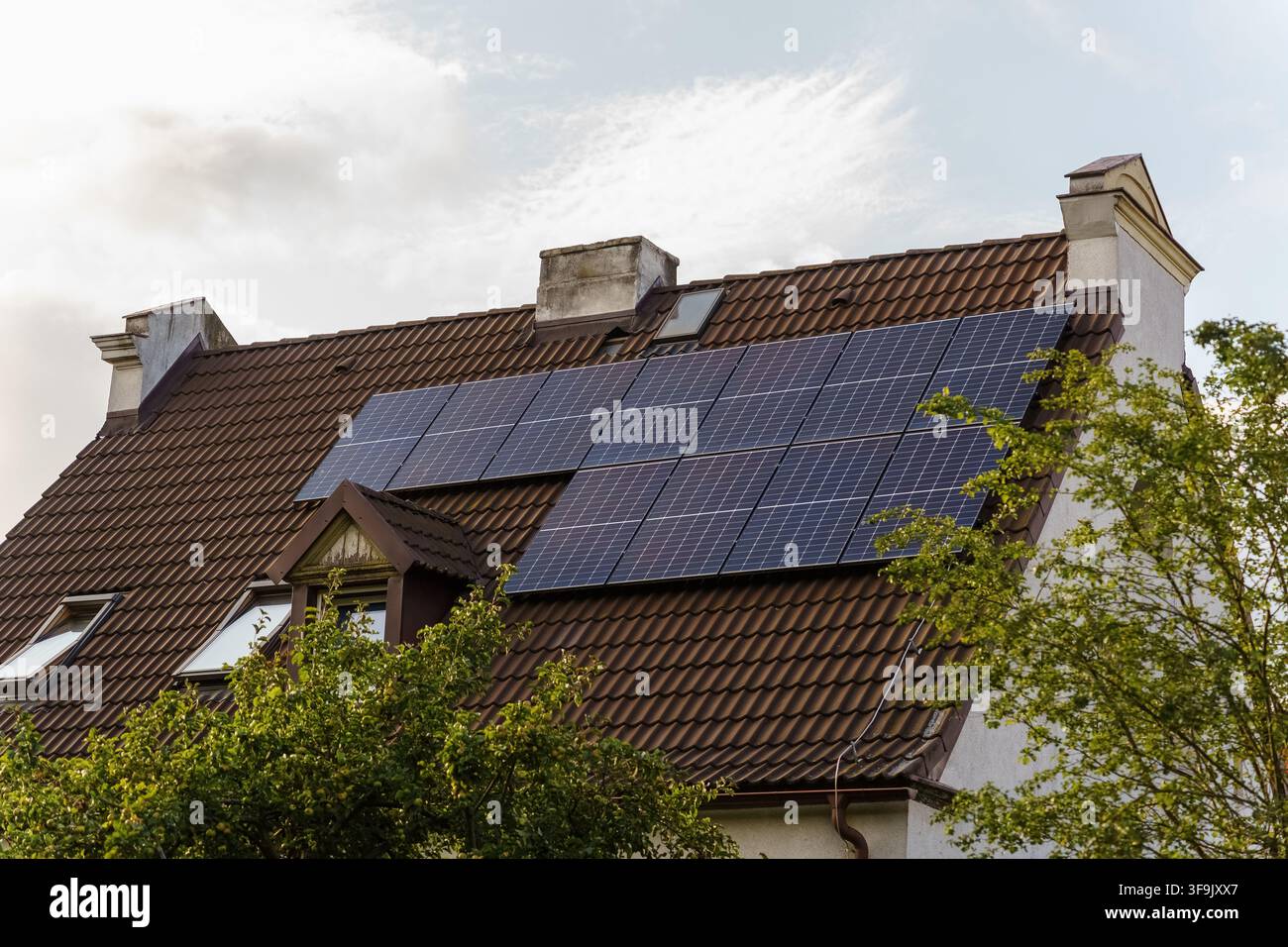 Panelli solari montati su un tetto di tegole marroni di una residenza sotto un cielo nuvoloso, rappresentanti soluzioni di energia sostenibile e miglioramento della casa Foto Stock