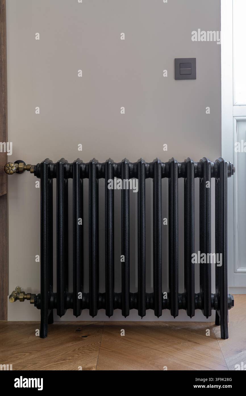 Radiatore in ghisa nera in un interno minimalista con pavimenti in legno e luce naturale, elemento riscaldante in stile vintage Foto Stock