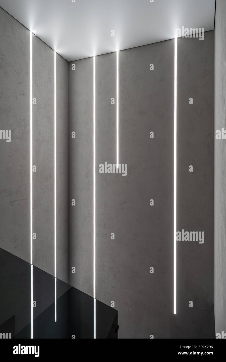 Vista verticale di un muro di cemento grigio con strisce luminose a LED, interno architettonico minimalista Foto Stock