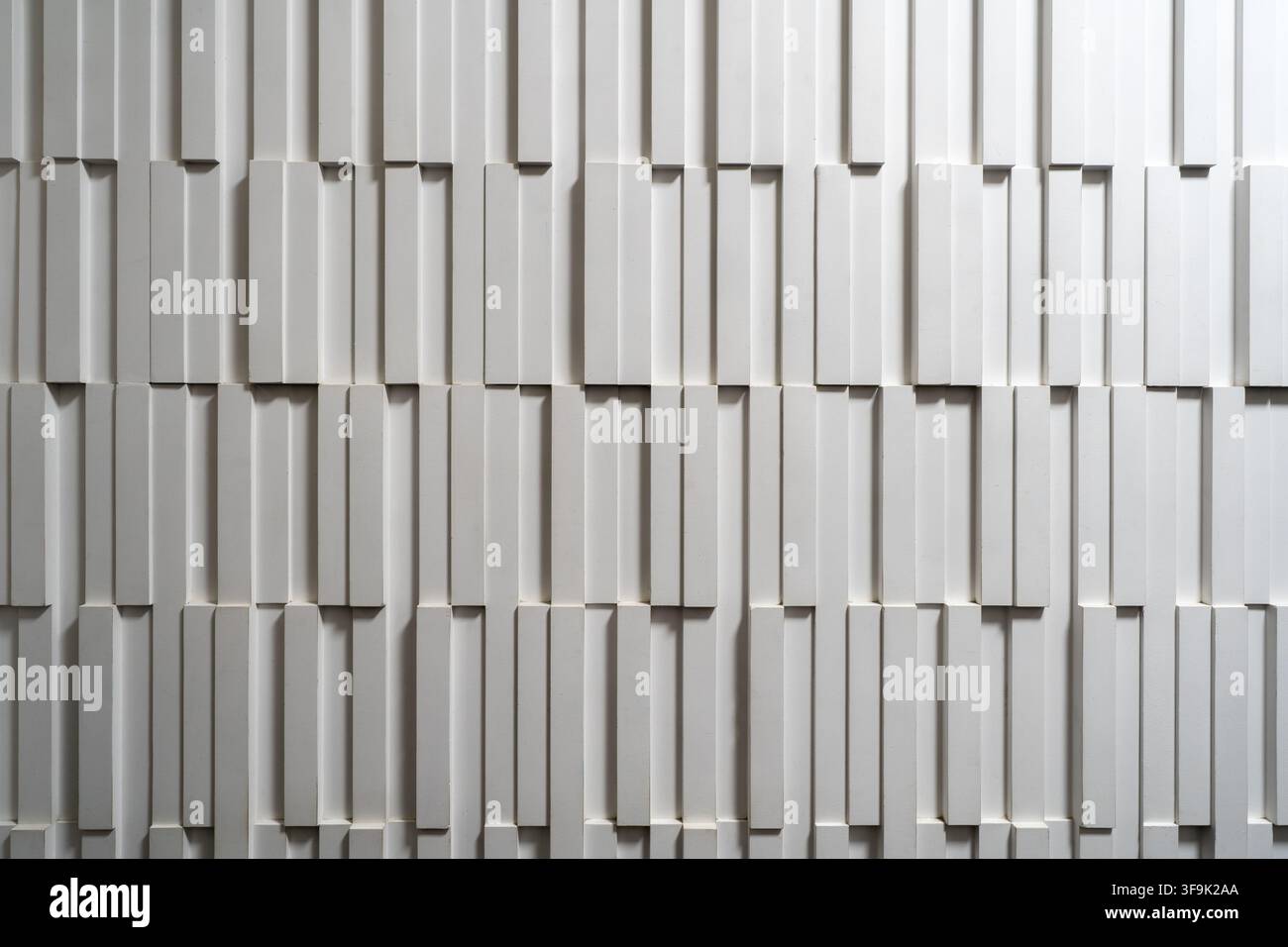 Muro bianco testurizzato contemporaneo con pannelli 3D geometrici disposti in un motivo verticale sfalsato, creando profondità, ombre e un architetto minimalista Foto Stock
