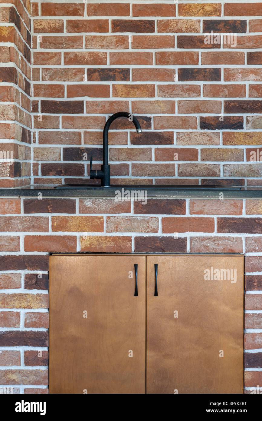 Lavandino da cucina all'aperto con rubinetto nero integrato in muro di mattoni rossi, mobile in legno sotto, dettaglio di design Foto Stock