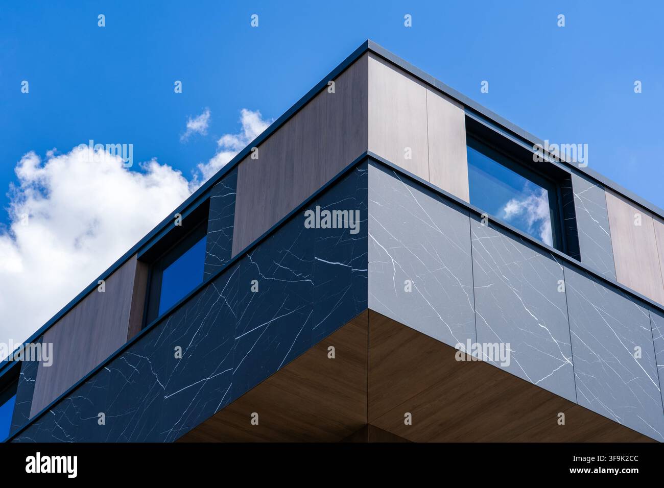 Angolo di edificio moderno con rivestimento in marmo nero e pannelli di legno contro il cielo blu, ripresa a basso angolo verso l'alto, fotografia architettonica con nuvole Foto Stock