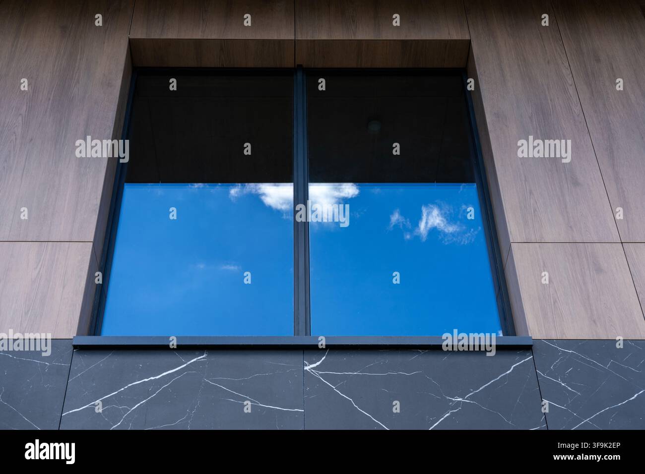 Edificio moderno con finestra a telaio nero e pannelli di vetro che riflettono un cielo nuvoloso, dettaglio di design esterno contemporaneo Foto Stock