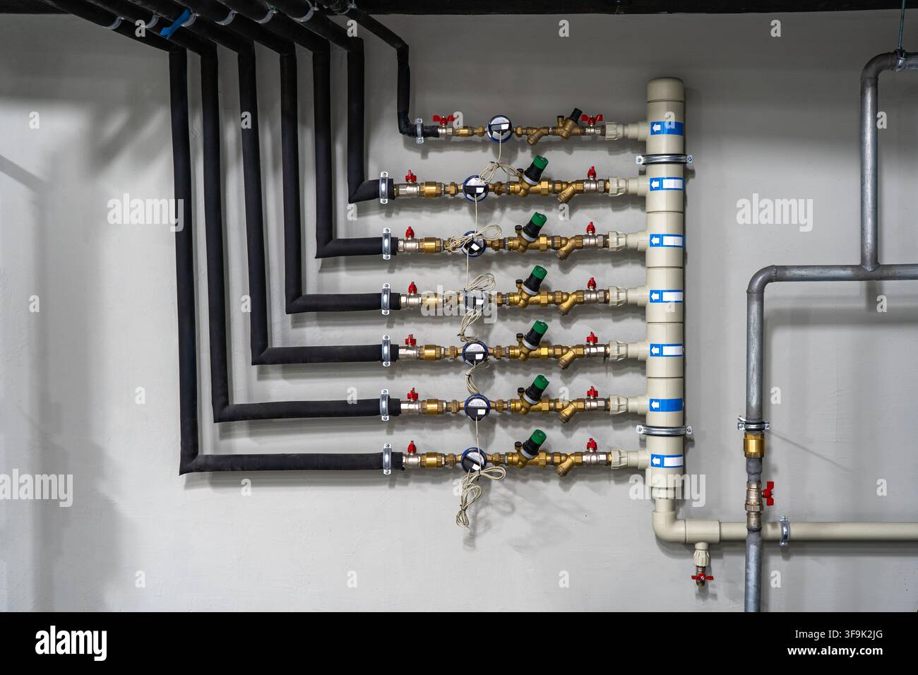 Sistema moderno di distribuzione dell'acqua residenziale con più tubi isolati, contatori dell'acqua, regolatori di pressione e valvole di intercettazione in una sala macchine Foto Stock