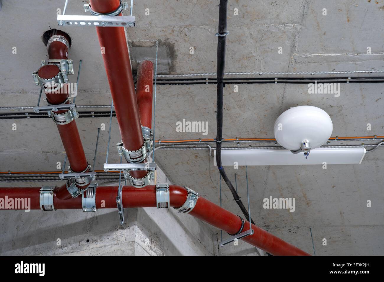 Protezione antincendio moderna e infrastrutture di servizio con tubi sprinkler rossi, condotti elettrici e sistemi meccanici montati a soffitto Foto Stock
