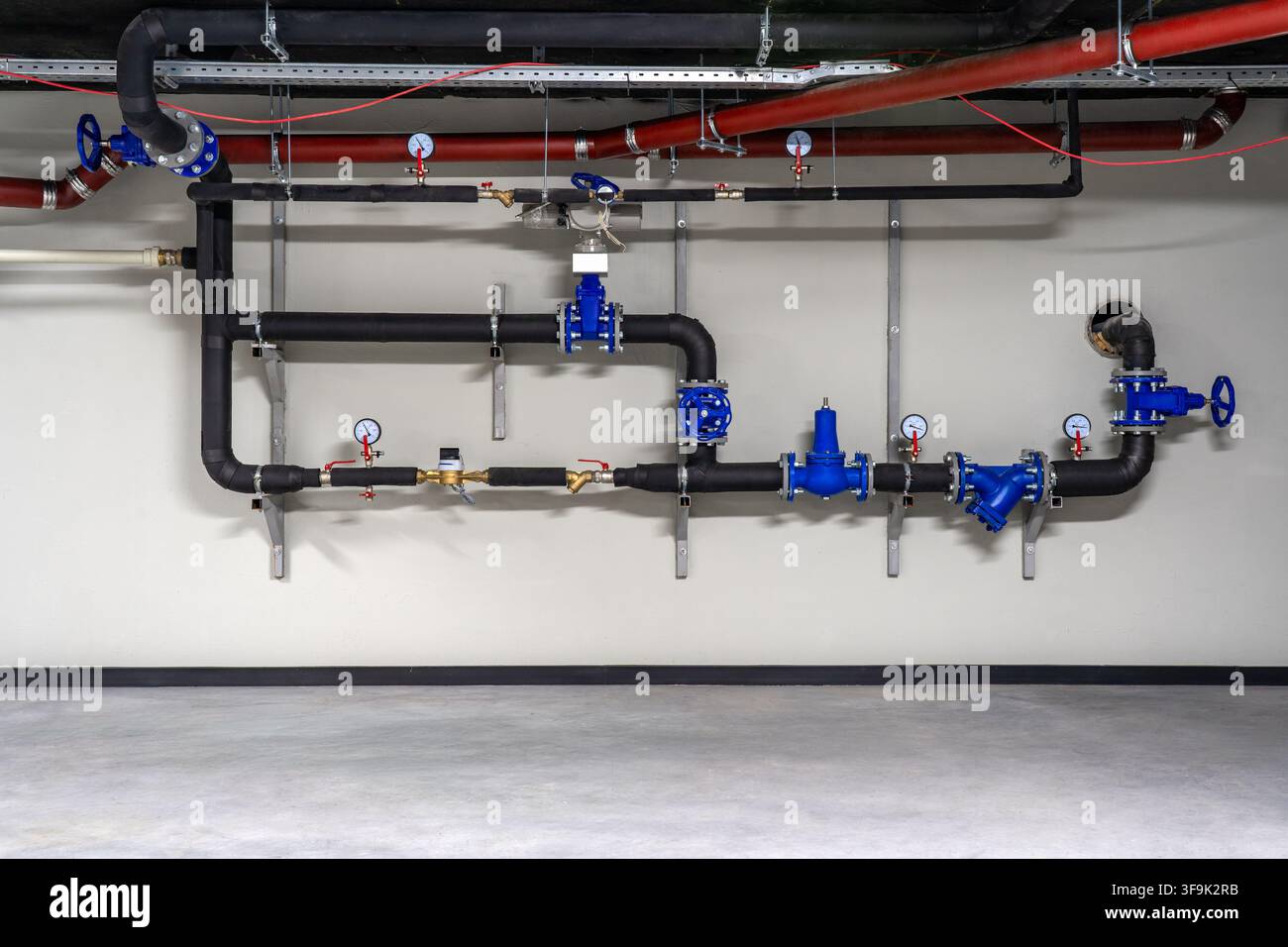 Infrastruttura idraulica di edifici commerciali con tubi dell'acqua isolati neri, valvole di controllo blu, manometri e sistema di filtraggio Foto Stock