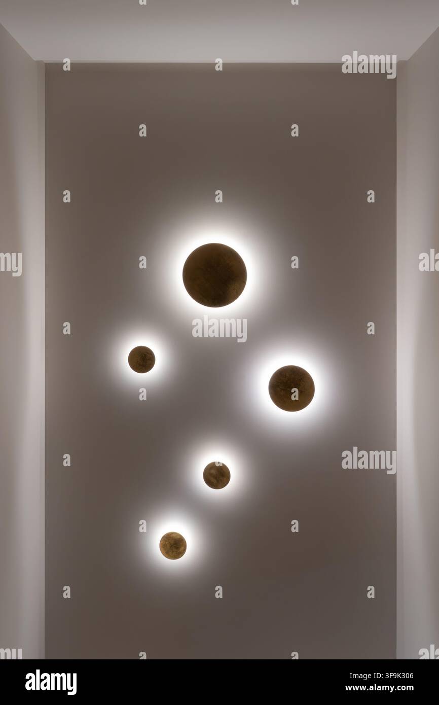 Interno architettonico moderno con cinque applique da parete decorative circolari con aloni luminosi su una superficie beige neutra Foto Stock