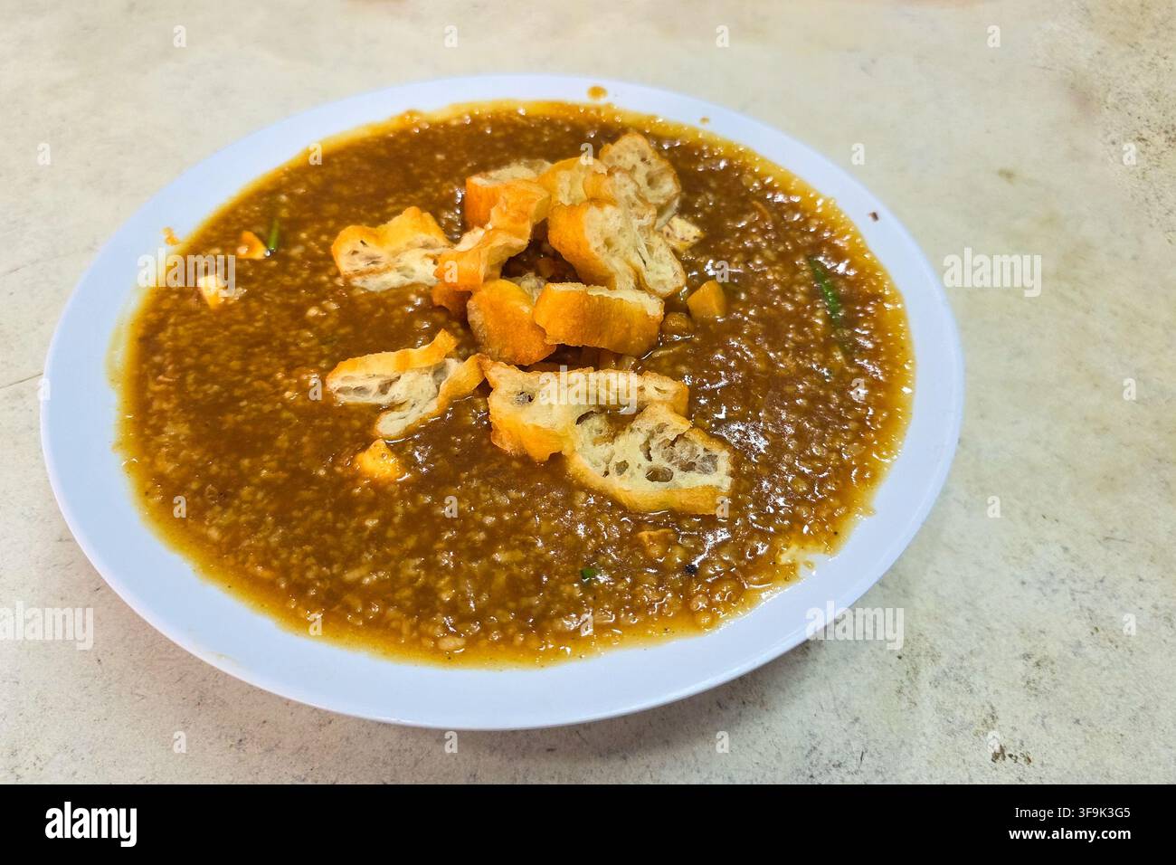 Primo piano di una ciotola di porridge di riso fritto o congee con guarnizione di bastoncino di pane fritto o you tiao, cibo comfort popolare a Klang, Malesia Foto Stock