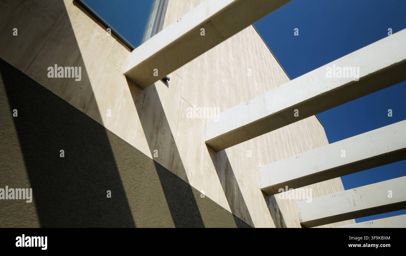 Facciata architettonica moderna con travi in cemento che proiettano ombre geometriche sotto un cielo blu terso Foto Stock