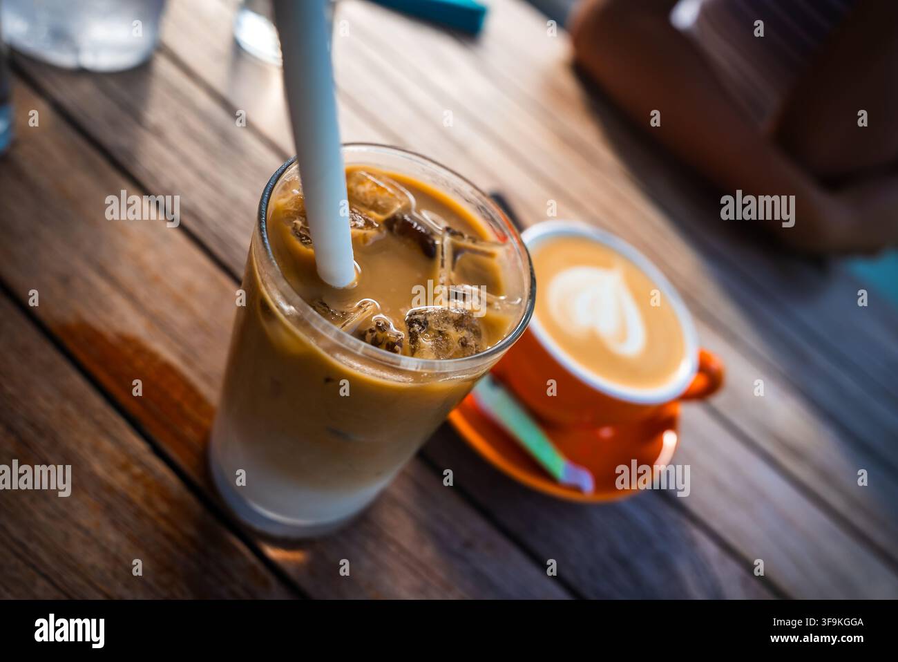 Cappuccino freddo con una cannuccia e caffè caldo in una tazza su un tavolo di legno Foto Stock