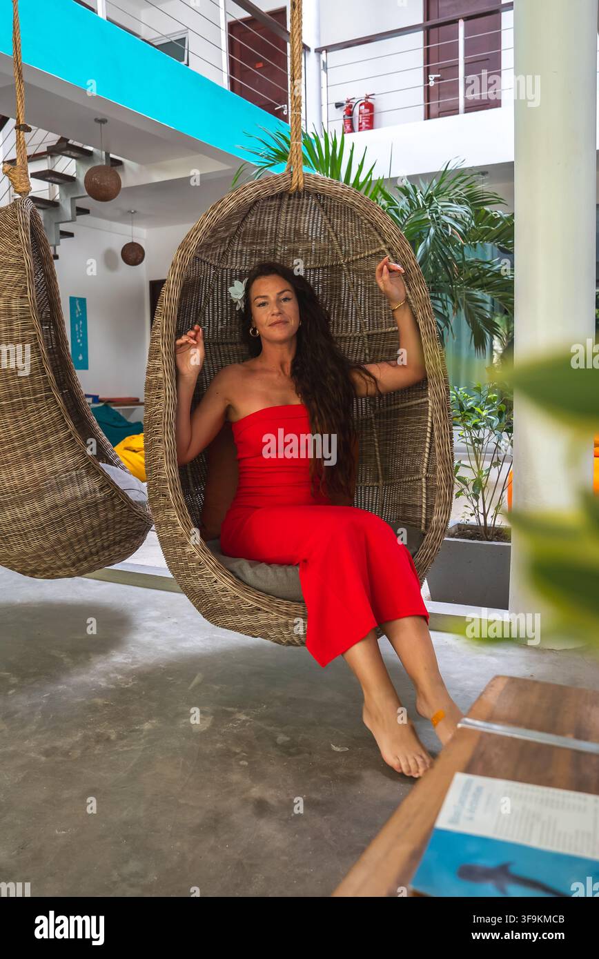 Donna seduta su una sedia a nido sospesa in vimini in un resort delle Maldive Foto Stock