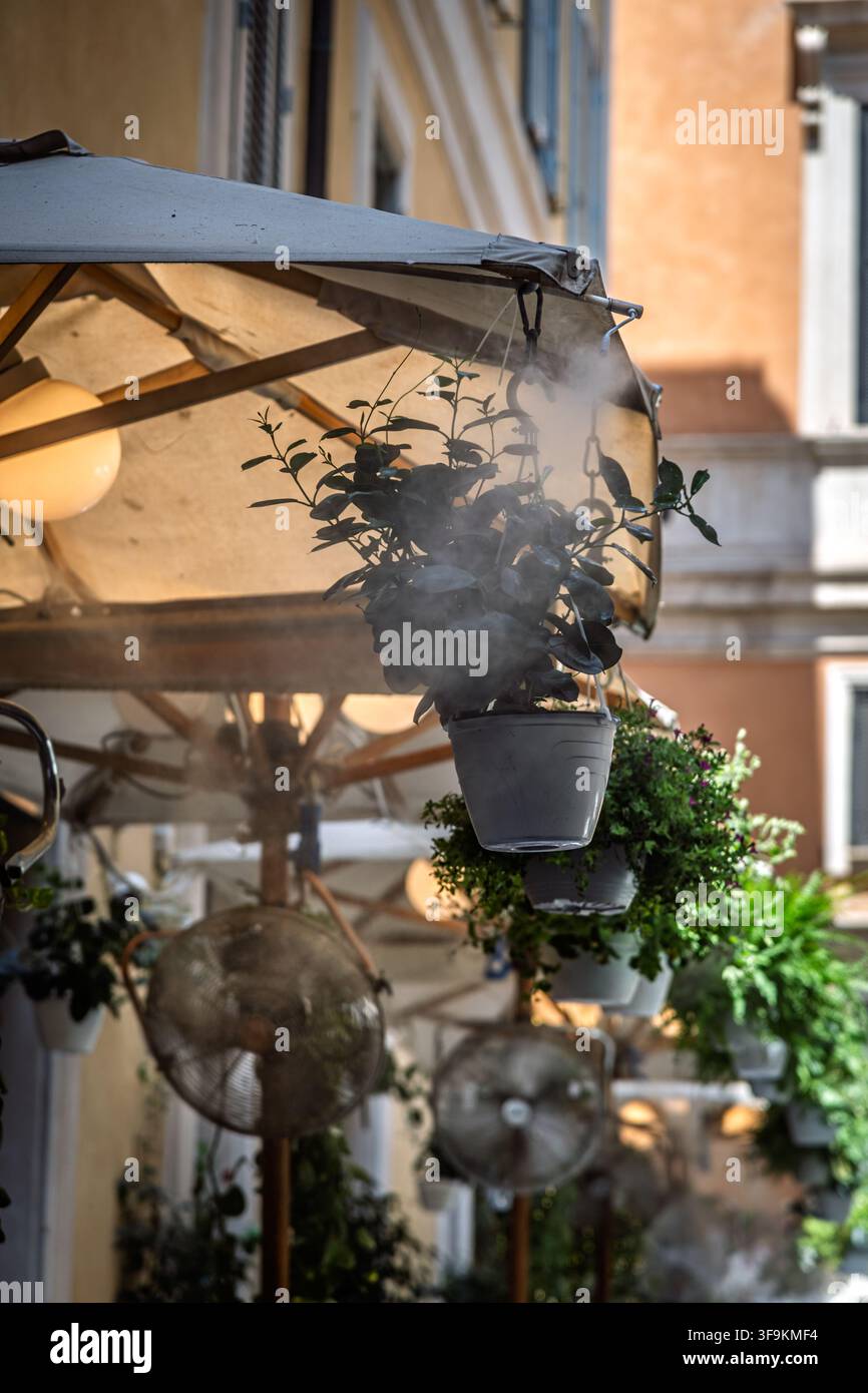 Un ristorante utilizza ugelli di spruzzatura a soffitto per spruzzare una fine nebbia rinfrescante sui commensali all'aperto durante un'ondata di caldo a Roma, Italia. Foto Stock