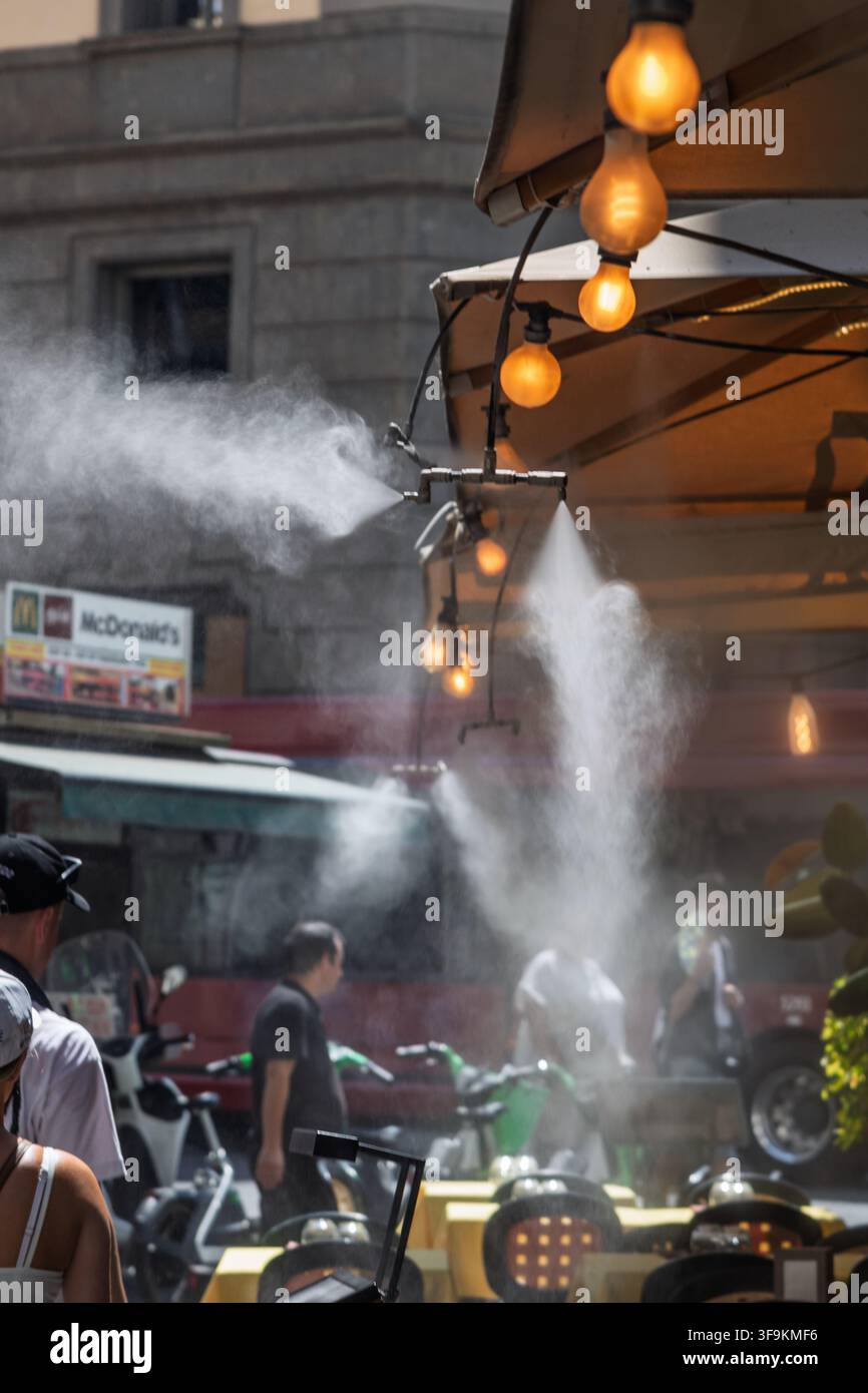 Un ristorante utilizza ugelli di spruzzatura a soffitto per spruzzare una fine nebbia rinfrescante sui commensali all'aperto durante un'ondata di caldo a Roma, Italia. Foto Stock