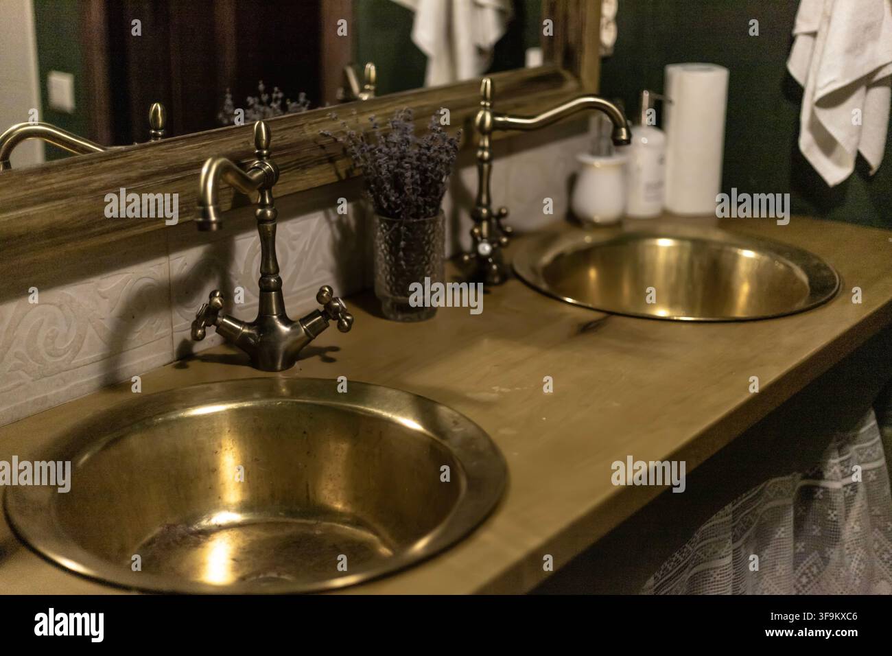 Interno di bagno rustico con due lavandini rotondi in ottone con rubinetti in bronzo antico, piano di lavoro in legno, specchio e fiori di lavanda essiccati. Foto Stock