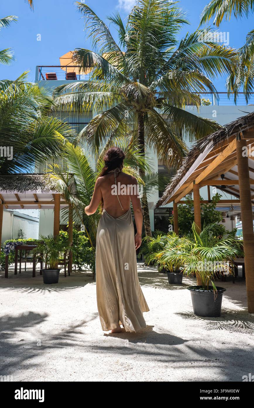 Donna in abito lungo che cammina attraverso il cortile di un resort alle Maldive Foto Stock