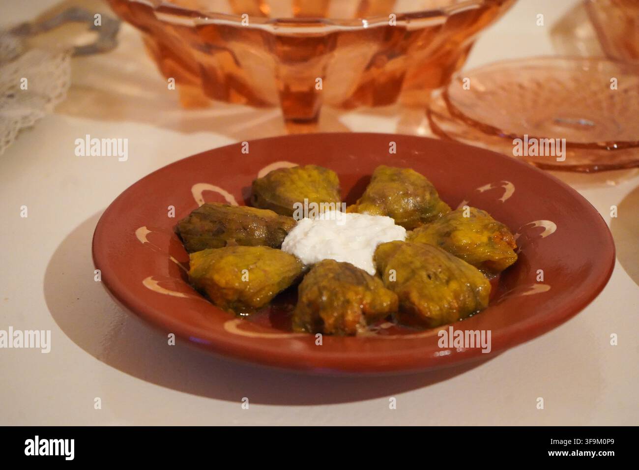 Una porzione di fiori di zucchina ripieni Anthoi, disposti radialmente su un piatto di terracotta marrone-rossastro, sormontati da una cucchiaiata di yogurt al centro. Foto Stock