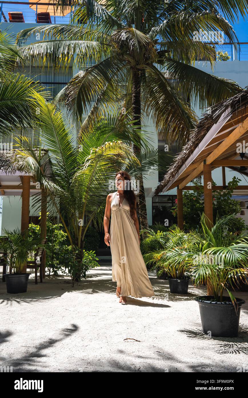 Donna in abito lungo che cammina attraverso un resort tropicale a Dhigurah, Maldive Foto Stock