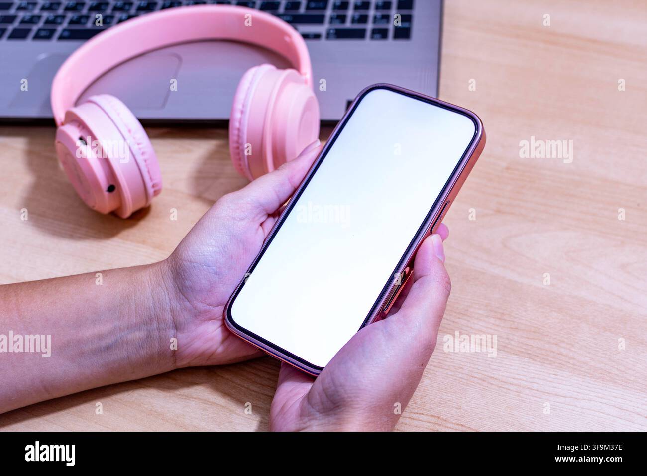 Una persona tiene un cellulare rosa con uno schermo bianco. Accanto al telefono c'è un paio di cuffie rosa Foto Stock