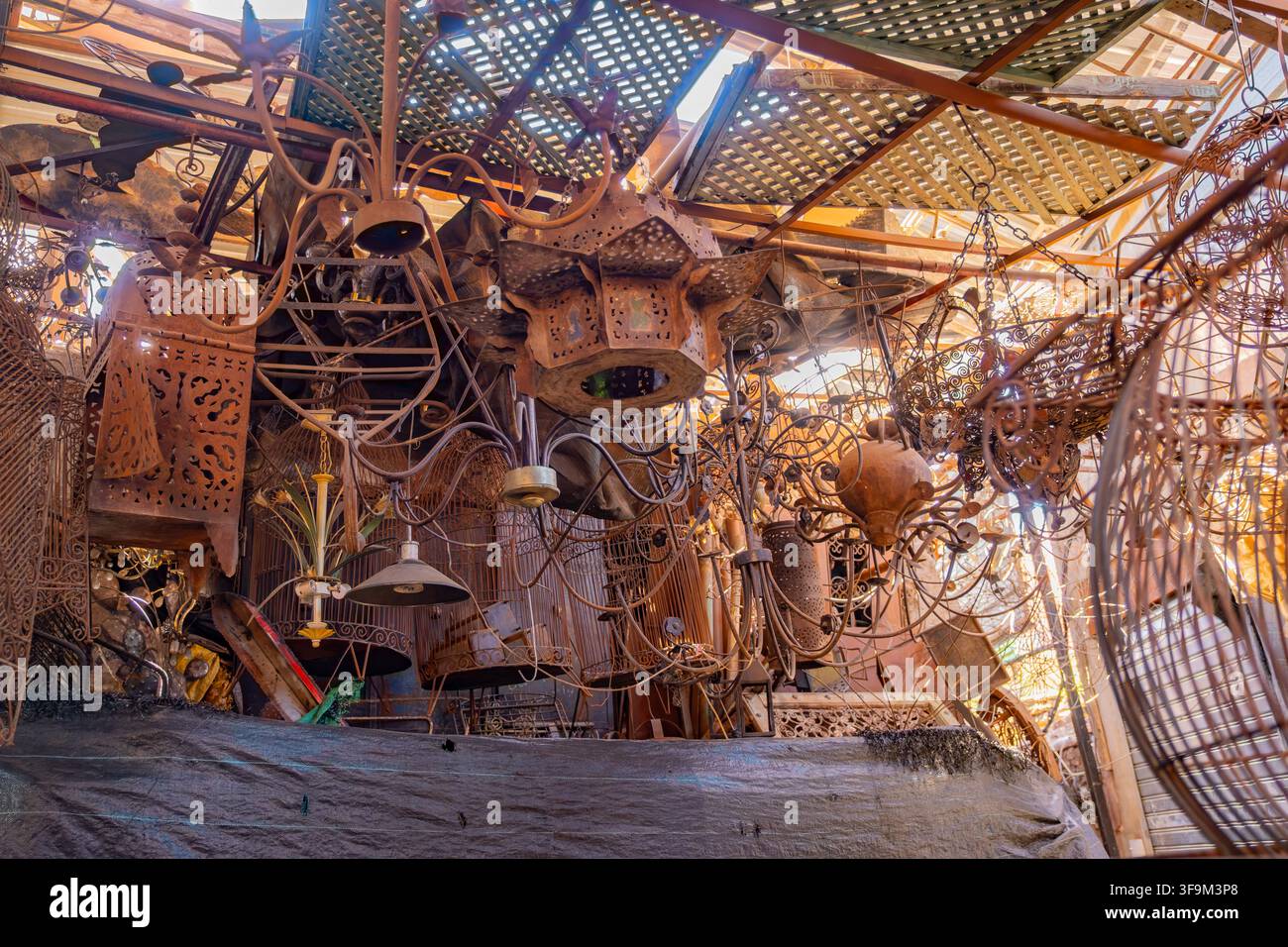 Lampade di ferro arrugginite, lampadari e oggetti in metallo appesi in un disordine caotico dal soffitto dentro una bottega di lavori metallici nel souk tradizionale della Medina a Marr Foto Stock