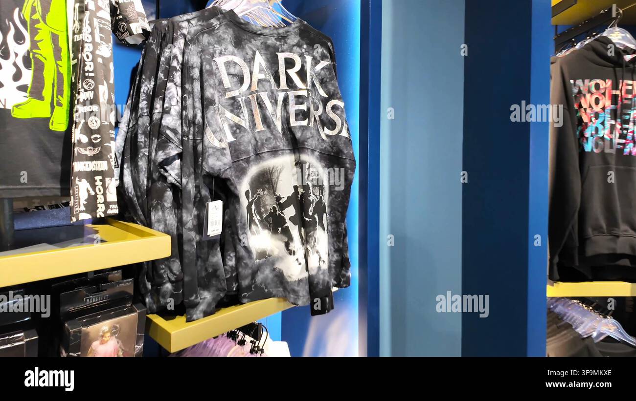 ORLANDO, FL, USA - 15 AGOSTO 2026: Una maglietta a maniche lunghe tie-dye a tema Dark Universe appesa in una vetrina di un negozio, con grafica ispirata al film sul retro Foto Stock