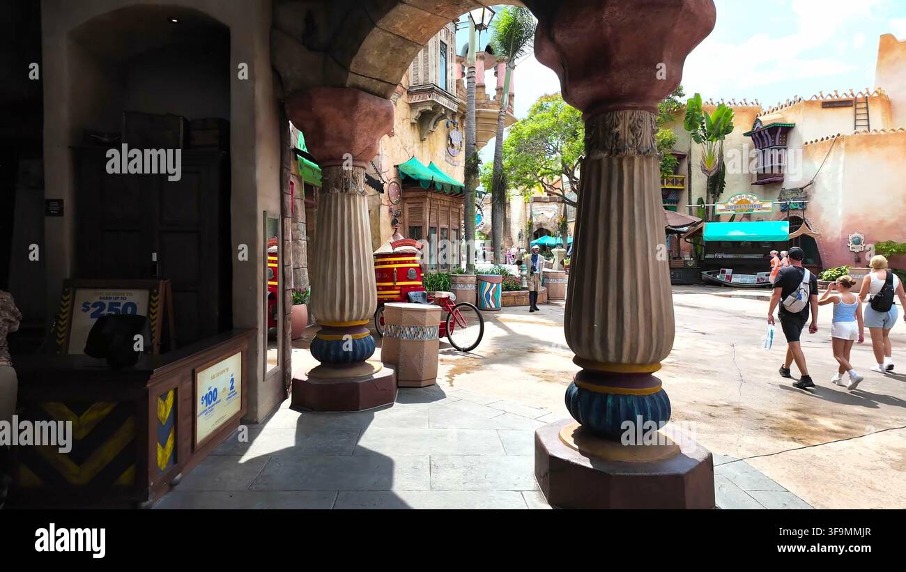 ORLANDO, FL, USA - 15 AGOSTO 2026: Vista attraverso un portale ad arco con colonne decorative che si affaccia su una passeggiata pedonale all'aperto soleggiata a un Foto Stock