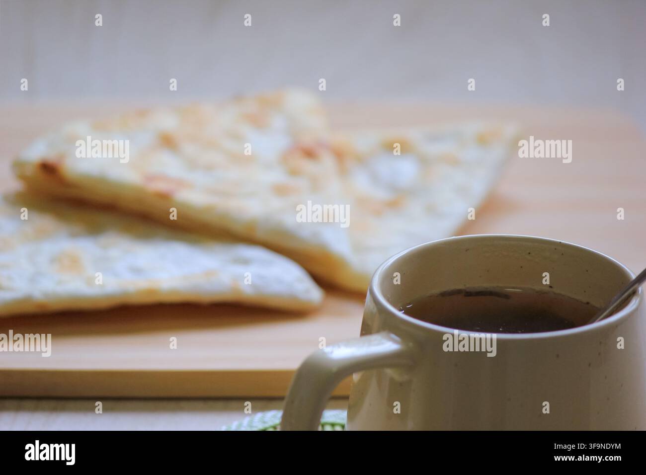 Spuntino mattutino accogliente con tè caldo in una tazza di ceramica e pane piatto friabile appena sfornato su una tavola di legno. Foto Stock
