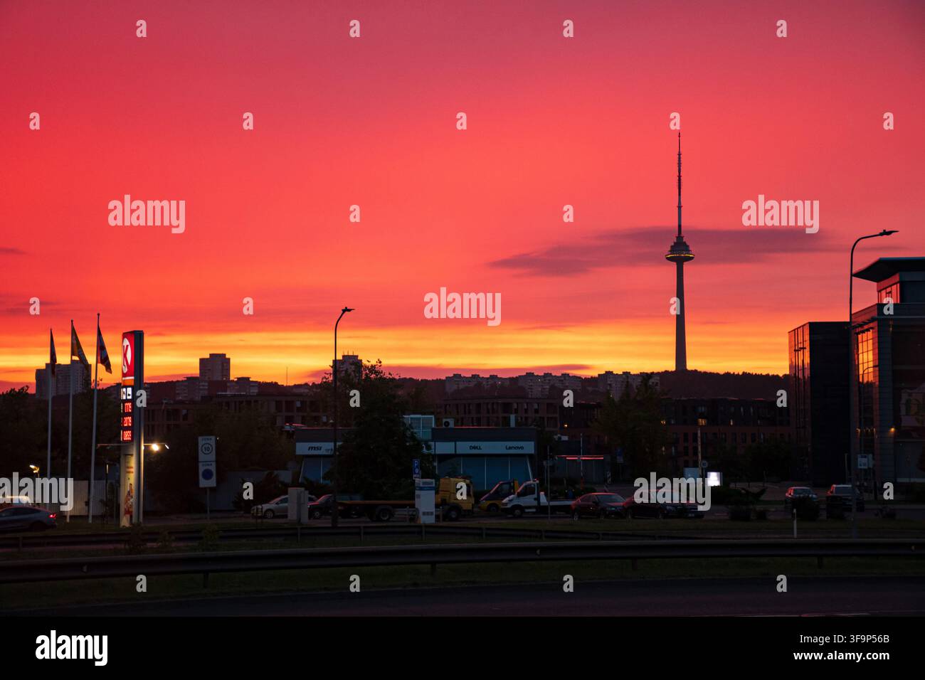 Un bellissimo tramonto sulla città di Vilnius, Lituania, con la silhouette della torre televisiva, di un edificio, di una stazione di servizio e di una strada Foto Stock