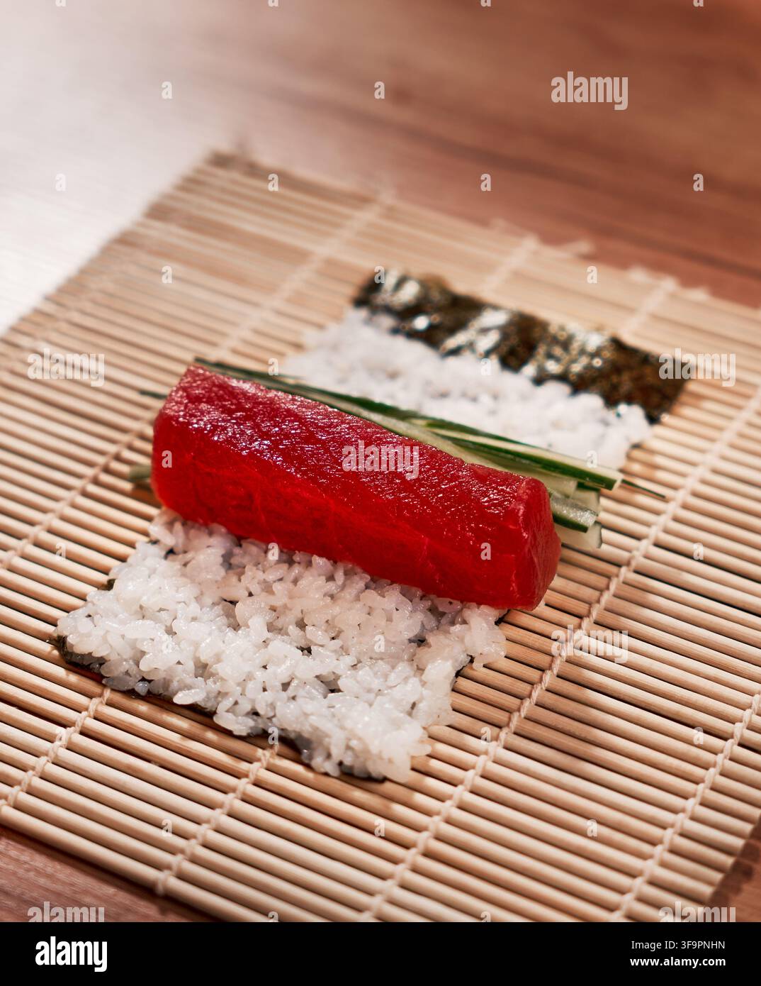 Preparazione di sushi con tonno fresco, cetriolo e riso su stuoia di bambù Foto Stock
