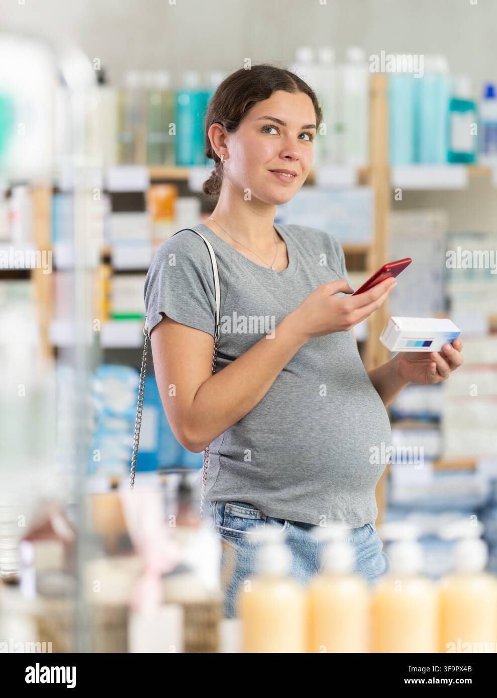 Attenta donna incinta che scansiona il codice QR per una scatola di unguento o gel in farmacia Foto Stock