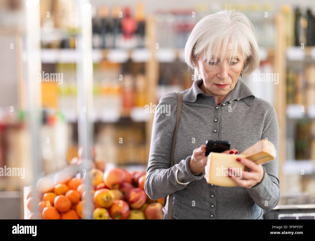 L'acquirente donna maturo scansiona il codice QR sull'etichetta del formaggio nel negozio di alimentari Foto Stock